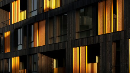 A modern apartment building with a dark wood facade and warm golden light filtering through the windows.