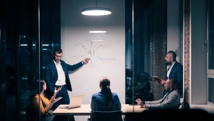 Diverse business team in modern office discussing AI with whiteboard.