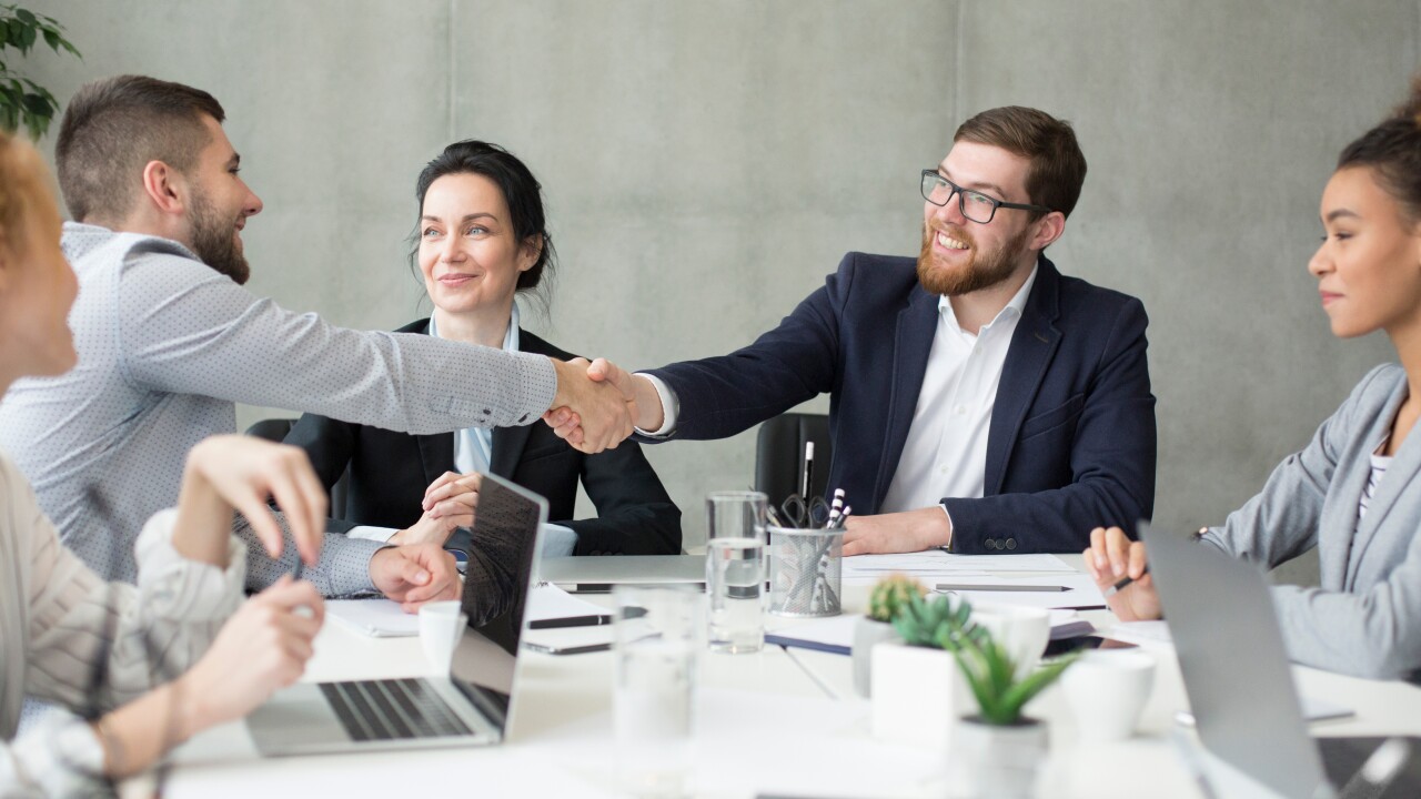 Two men shaking hands during meeting with coworkers
