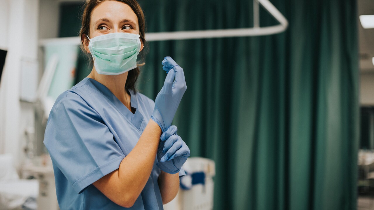 The nurse puts on gloves in a hospital room.