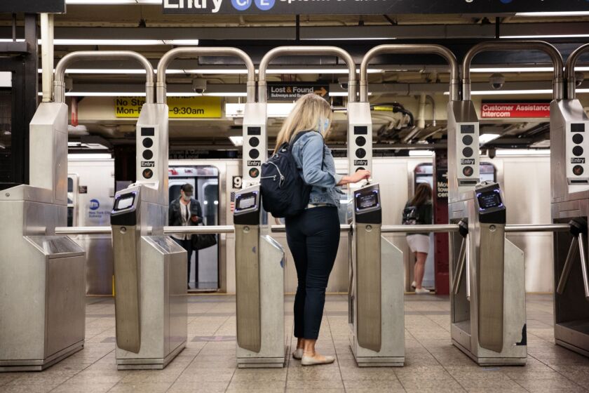 A commuter wearing a protective mask swipes a metro card through a turnstile slot at a subway station in New York