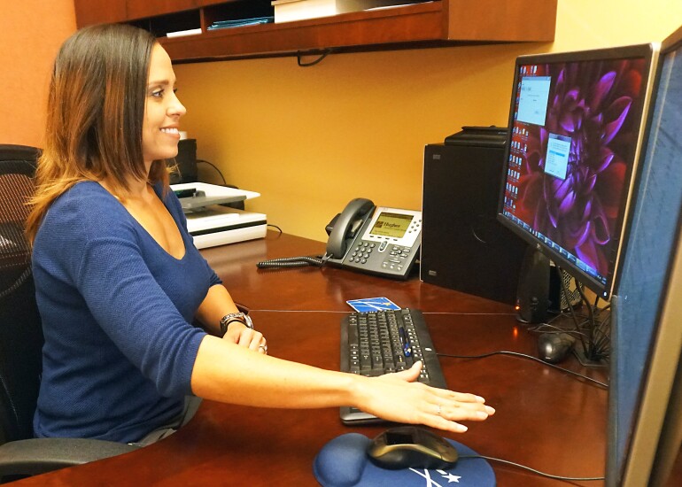 Hughes Federal Credit Union Manager Mary Burruel using a Verifast palm-biometric mouse to authenticate at her desk.