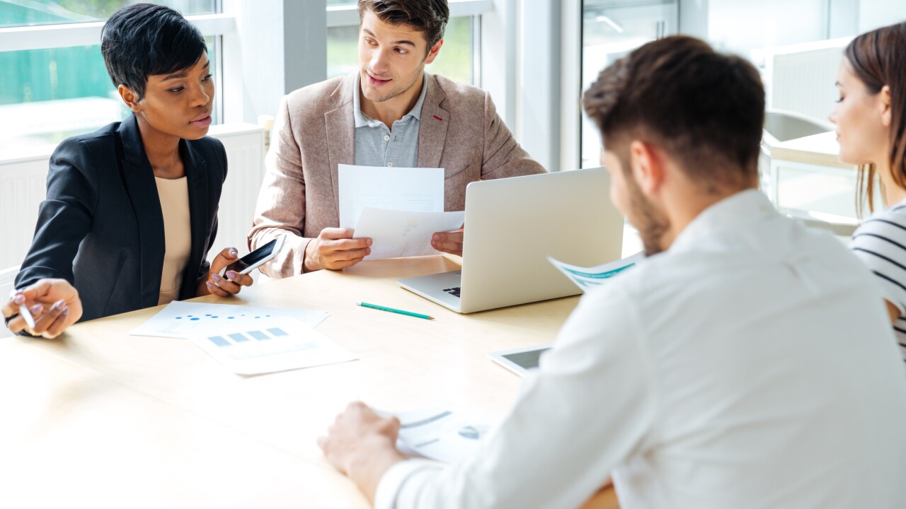 Employees sitting around table working, one with laptop