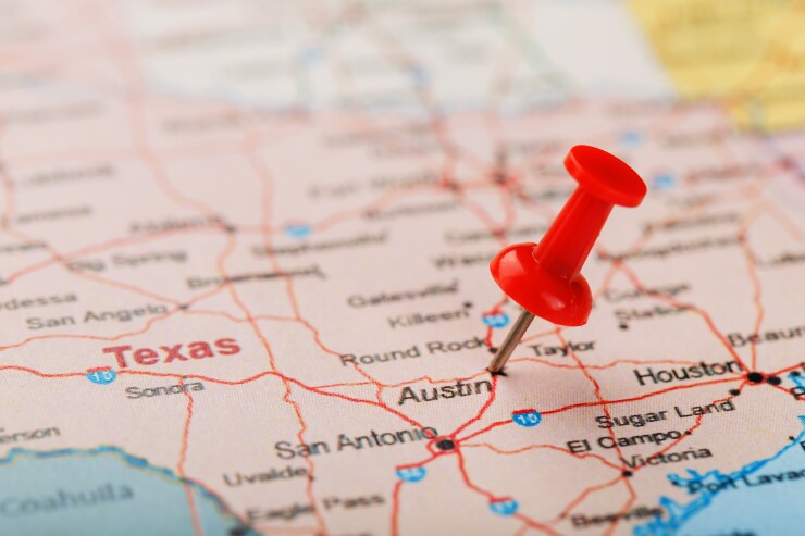 A thumb tack pinned into the city of Austin, Texas on a paper map.