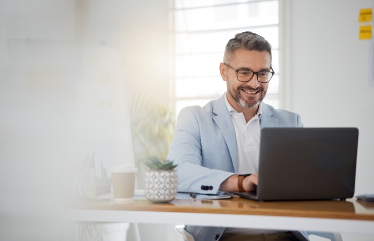 A middle-aged white man looks excitedly at his laptop at his desk. 