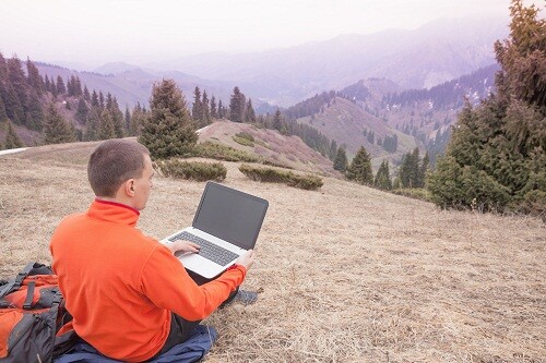 man dressed in red sweater uses laptop remotely with 3g or 4g network wireless at mountain, square orientation