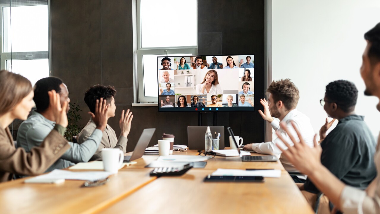 A group of people waving at a screen with other people calling in remotely.