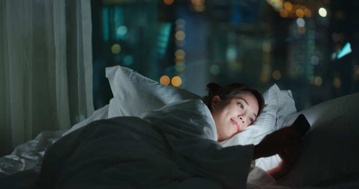 Woman laying in bed on phone, smiling