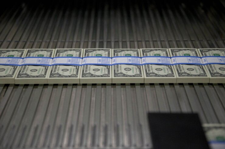 One dollar notes travel through a large examining packaging equipment machine after receiving a $100 currency strap and being cut.