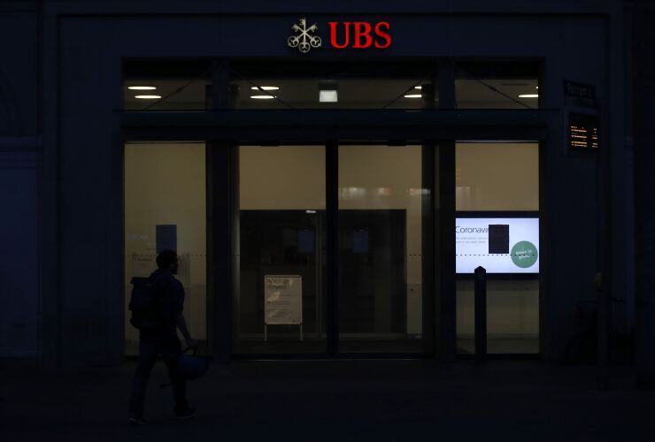 An illuminated logo sits on display above the entrance to a UBS Group AG bank branch at night in Bern, Switzerland, on Sunday, April 19, 2020. A UBS appeal of a record 4.5 billion-euro ($4.9 billion) French fine for helping clients stash undeclared funds in offshore accounts was postponed over concerns related to coronavirus pandemic, according to people familiar with the case.Photographer: Stefan Wermuth/Bloomberg