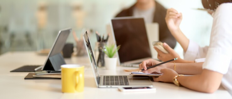 People working together at a table with laptops, coffee cups and writing materials