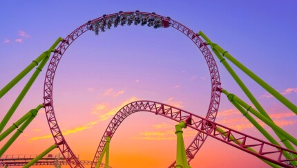 A rollercoaster with the people in an upside-down loop at sunset