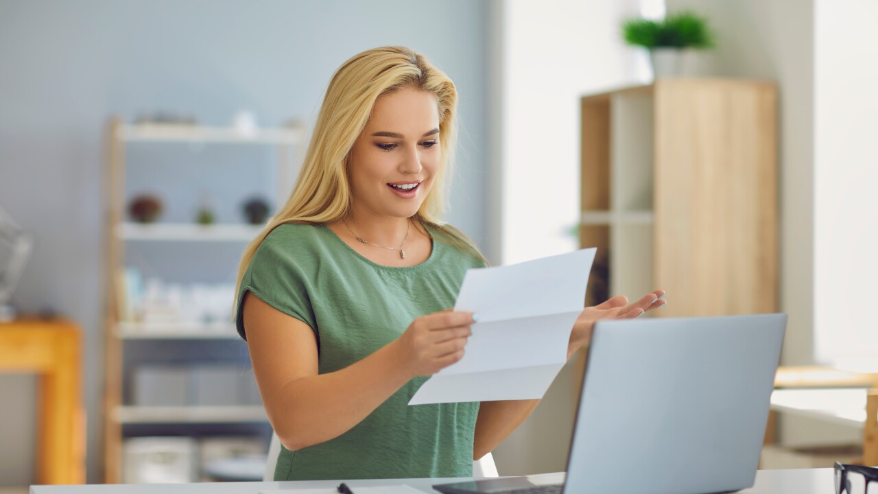 Woman looking at paper sitting in front of laptop