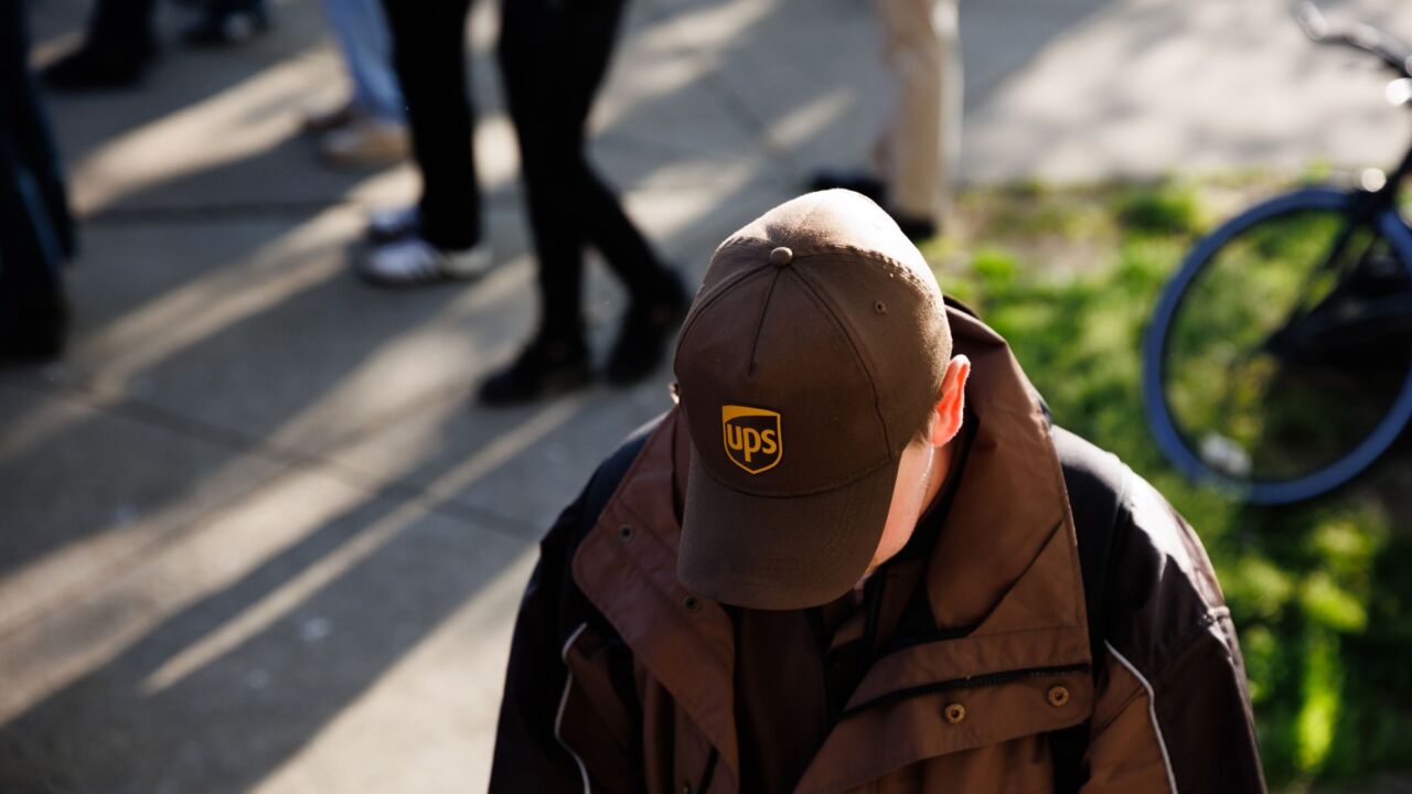 A man in a UPS cap with his head down, a busy street in the background.