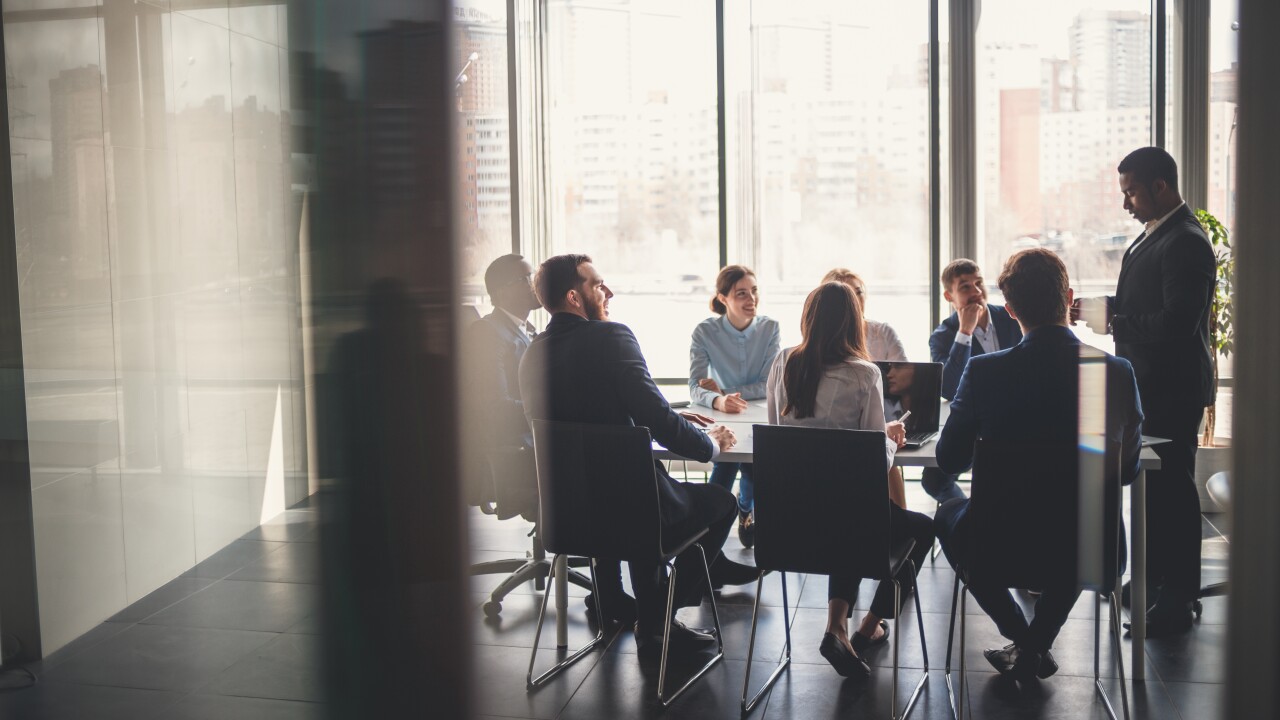 People sitting at a conference table while one person stands at an end of it.