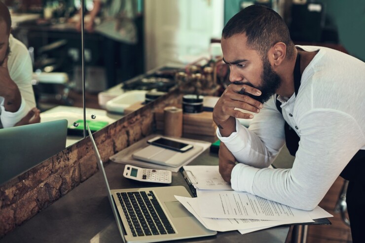 Man carefully studying a laptop computer screen with papers in front of him.