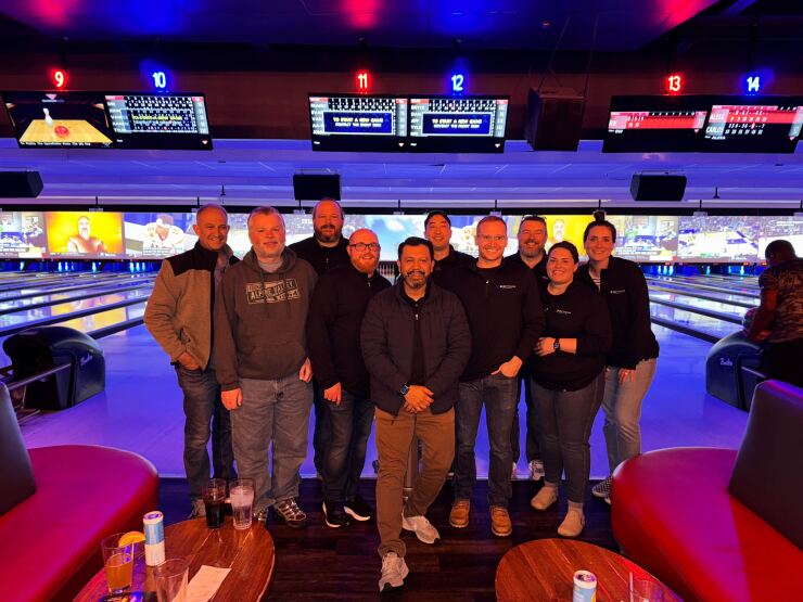 IOU Financial employees pose for a photo at a red-lit bowling alley.