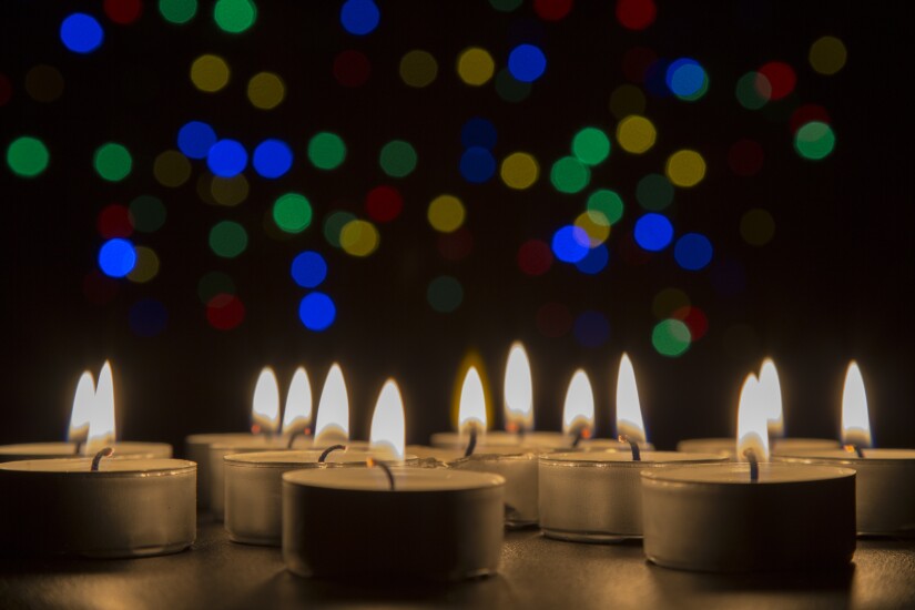 Tiny candles igniting together in the dark with lights shining in the background