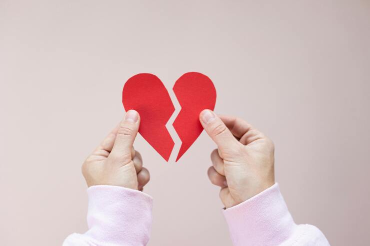 Female hands holding a paper heart with a crack down the middle of it