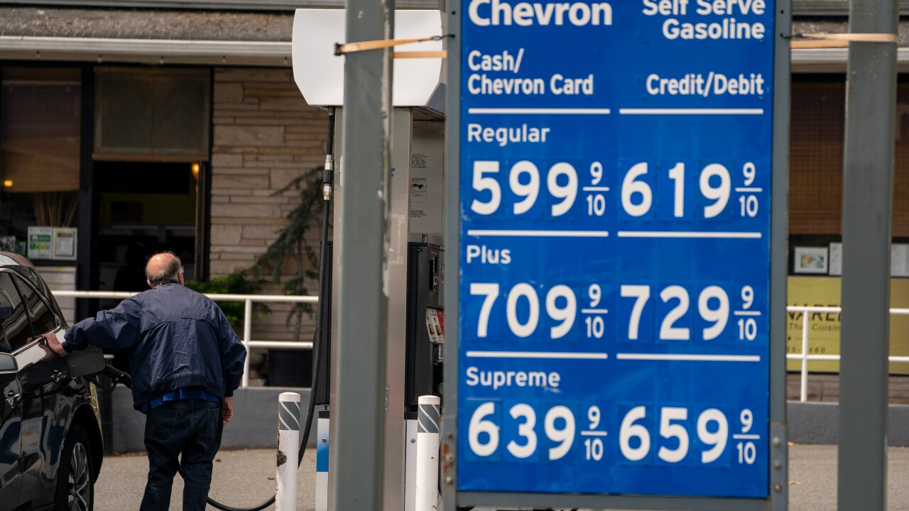 A picture of a man pumping gas next to a sign displaying the prices for gas.