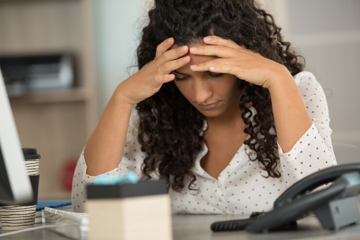 A woman puts her head in her hands in frustration at her desk.