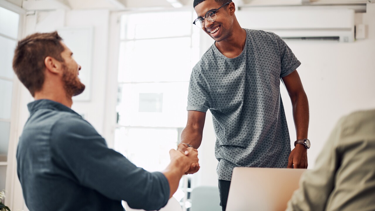 Young male standing up shaking hands with man sitting