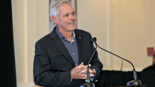 Javier D. Ferrer, the president and chief operating officer of Popular Inc., smiling with his hands crossed in front of a podium microphone.