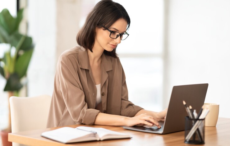 Woman working on laptop at desk, plant in background