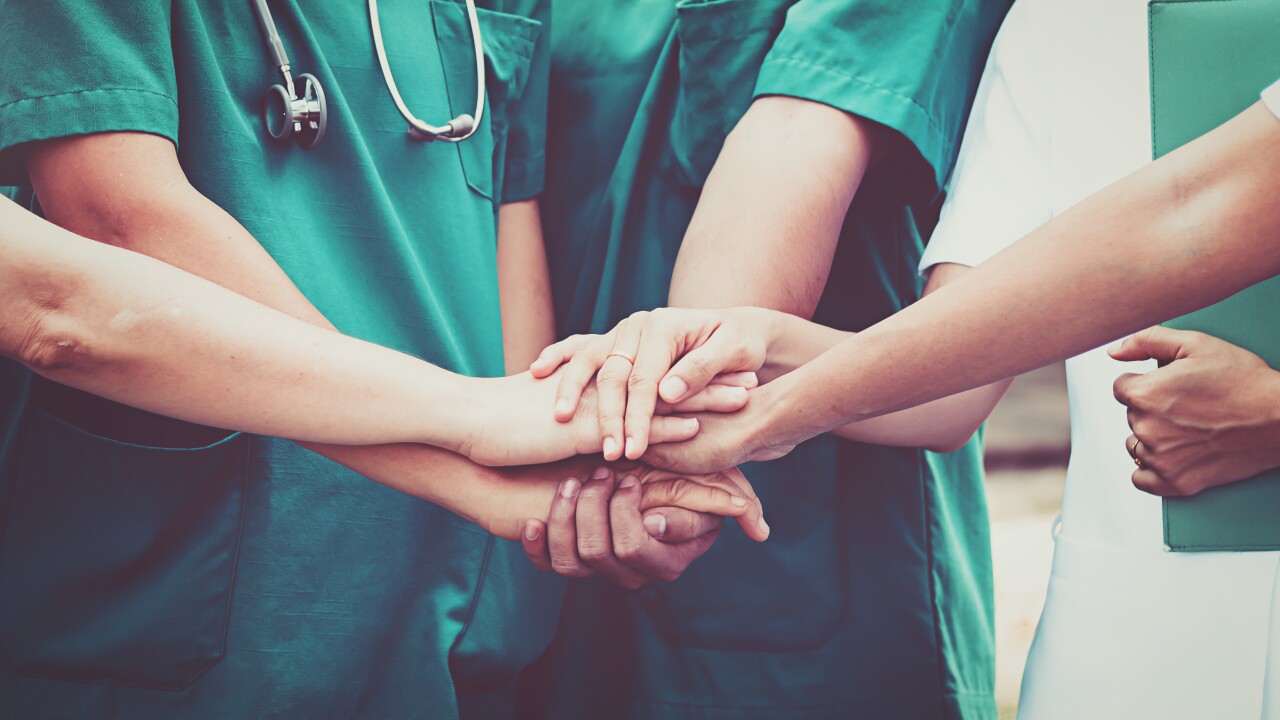 Nurses place their hands on top of each other, in a show of teamwork.