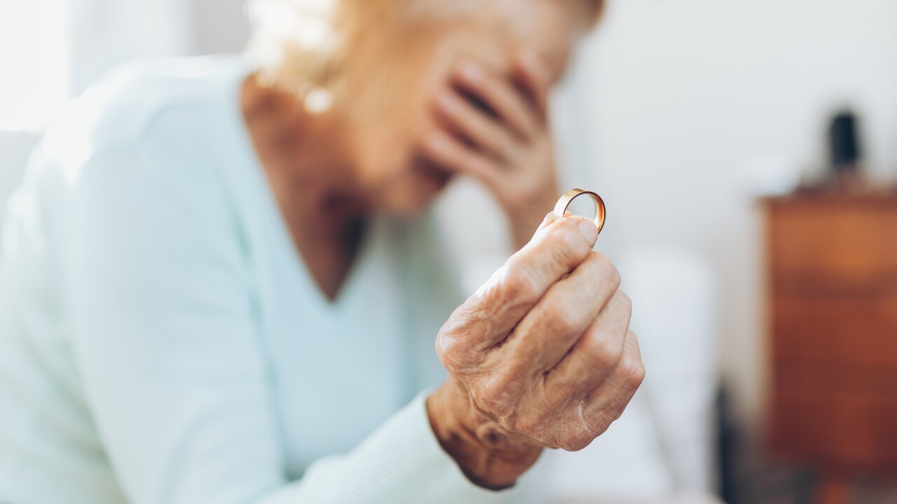 Heartbroken elderly woman holding a wedding ring - gray divorce