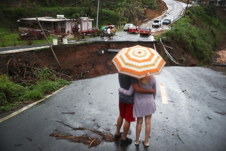 People look on at a section of a road that collapsed and continues to erode days after Hurricane Maria swept through Puerto Rico.
