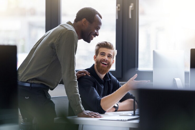 Two colleagues are laughing while looking at something on the desktop computer