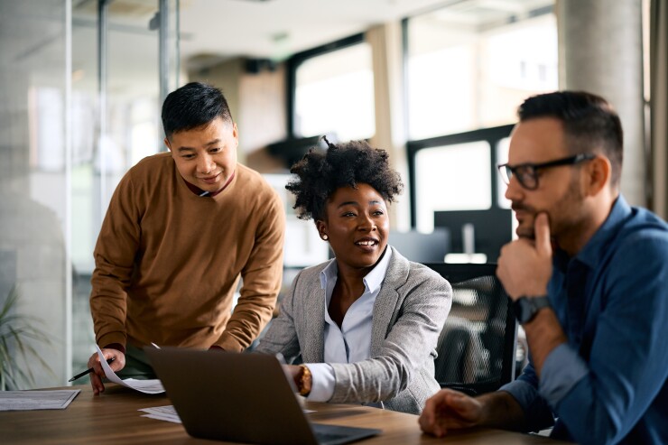 Three coworkers are sitting at a conference table discussing something they are looking at on paper.