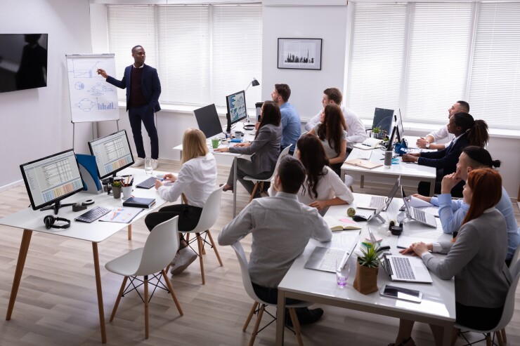 Man standing in front of room with chart, talking to group of professionals in office