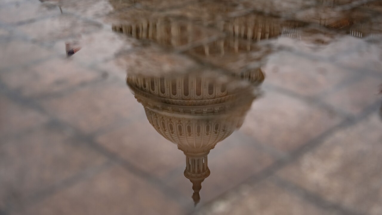 A reflection of the U.S. Capitol building is shown by a puddle outside of the building