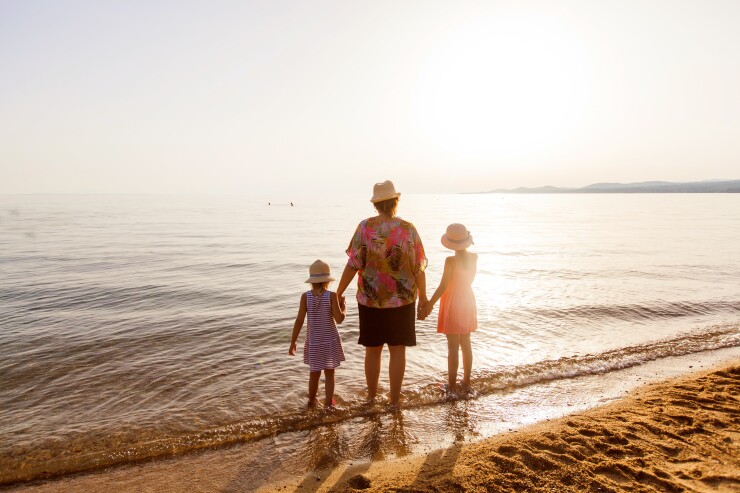 Family standing at edge of ocean holding hands, sunset, vacation