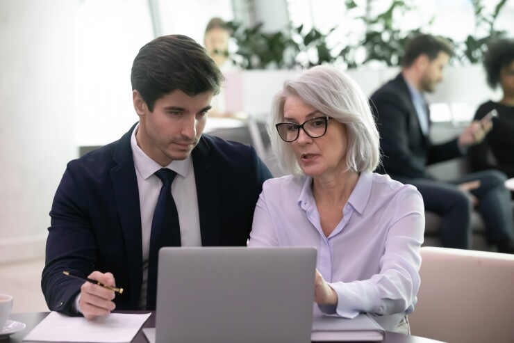 Older female and younger male employee looking at laptop working together