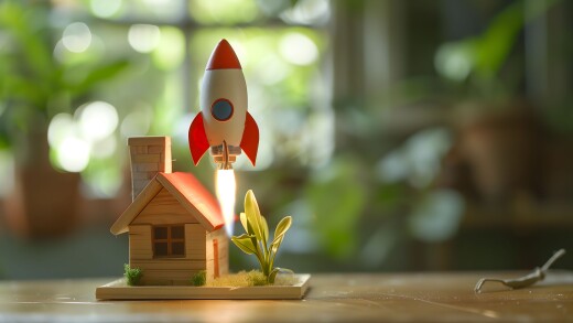 Miniature wooden house with a toy rocket launching behind it, symbolizing real estate growth, property value increase, or successful mortgage loan.