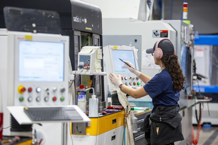 A woman with headphones on is touching a screen in the middle of what looks like a factory.
