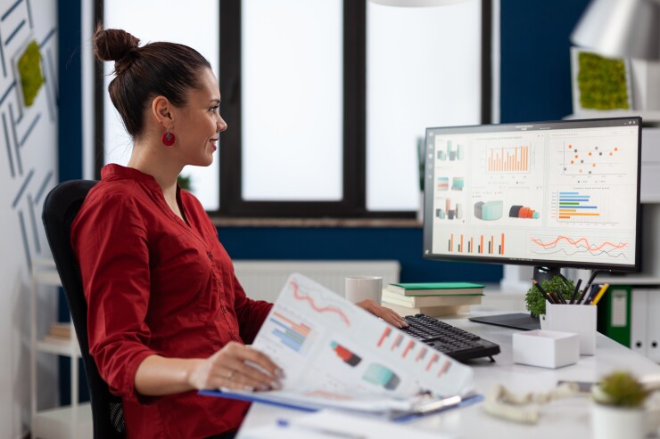 Woman sitting at desk wearing red shirt looking at computer with data
