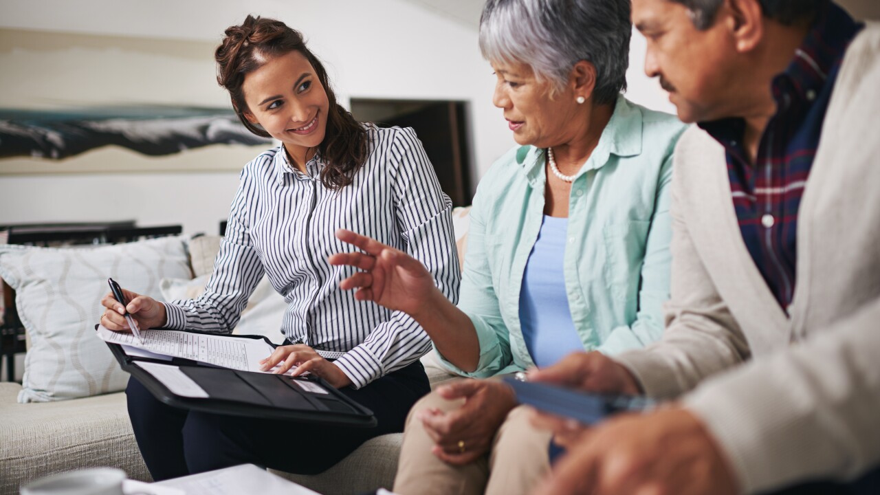 Senior couple speaking with advisor, looking at financial and insurance papers.