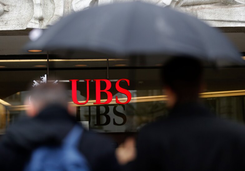 A pedestrian shelters under an umbrella while passing a UBS Group bank branch in Zurich, Switzerland.