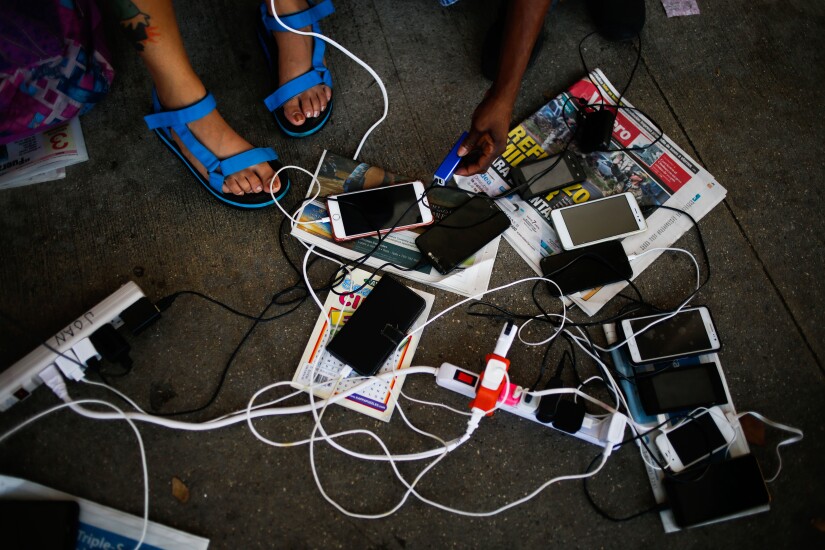 People charge their mobile devices outside a Wal-Mart Stores Inc. location in San Juan, Puerto Rico, on Thursday, Sept. 28, 2017.