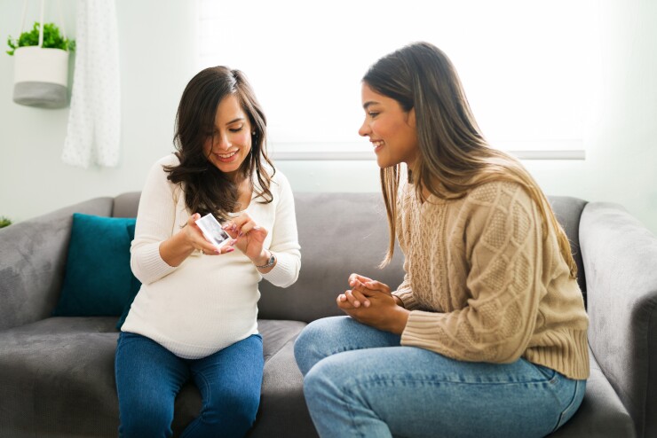 Two women sitting on couch, one woman pregnant, looking at sonogram