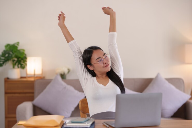 Woman stretching sitting down with eyes closed in front of laptop